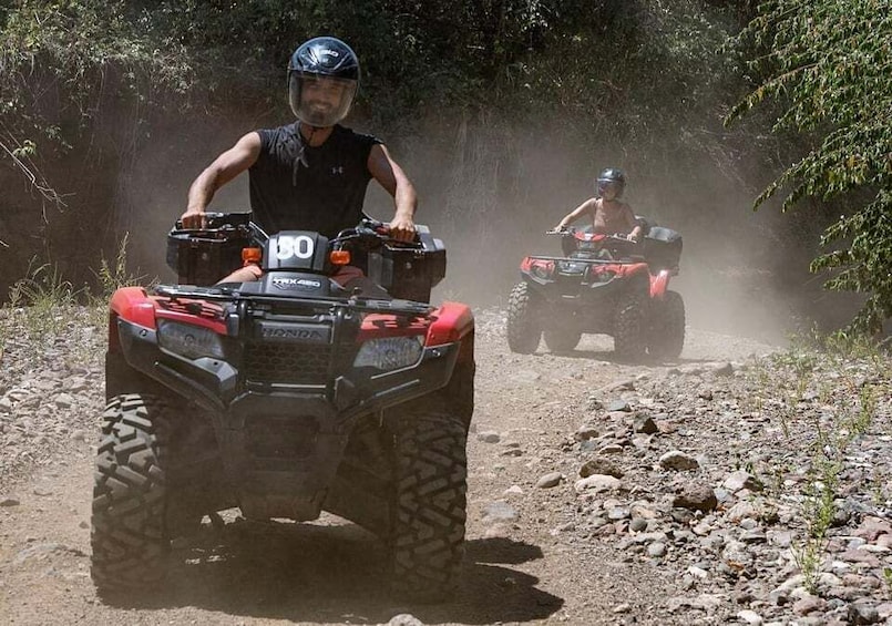 Twee personen rijden op quadbikes over een rotsachtige weg, omgeven door bomen. 1