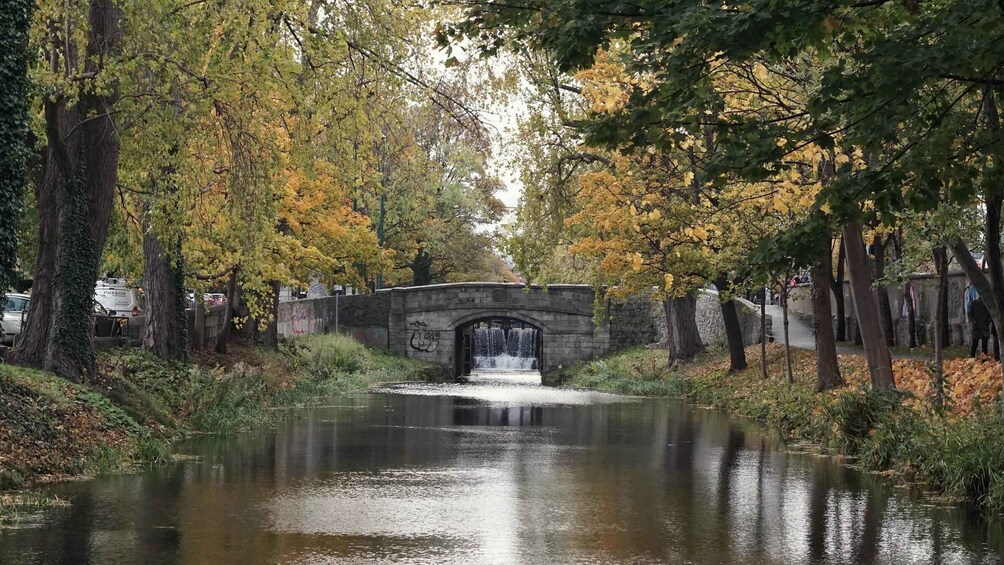 A stone bridge over a calm river with autumn foliage. 2