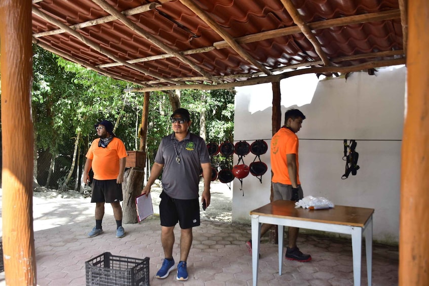 Three people in an outdoor setting with a covered area, a table, and helmets on the wall. 4