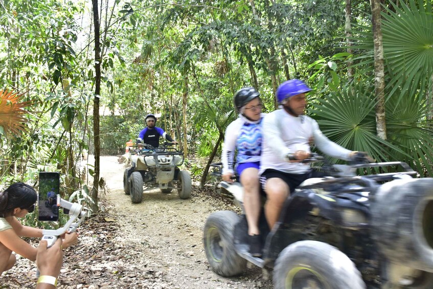 People riding atv's on a dirt path surrounded by trees. 5