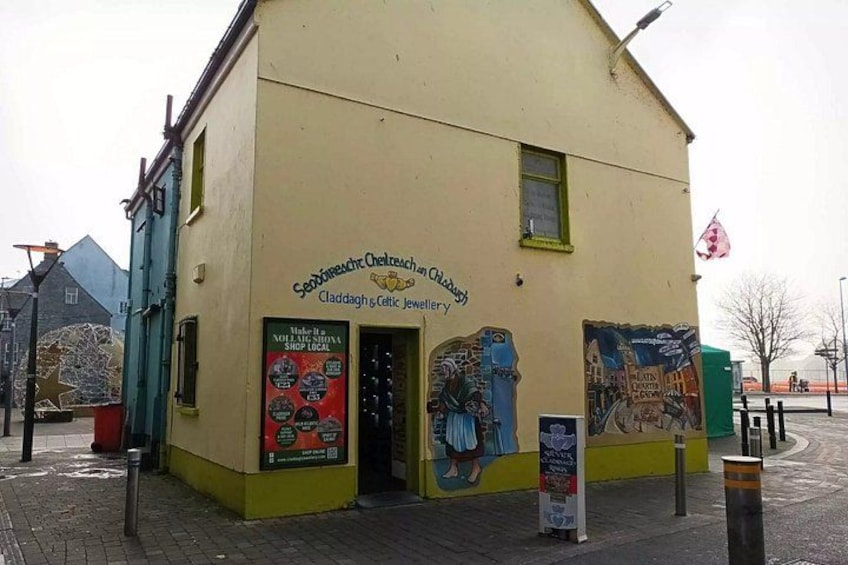 A building with a sign for 'Seasideche Chelrechain & Claddagh Jewellery' and a poster advertising local shops. 2