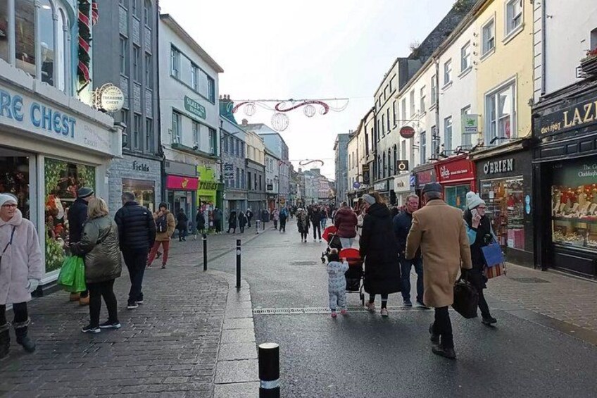 A busy street with pedestrians, shops, and a wet pavement. 4