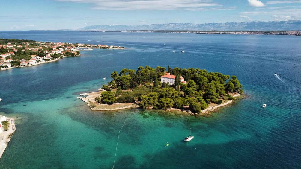 An island with a white building surrounded by trees and clear blue waters. 3