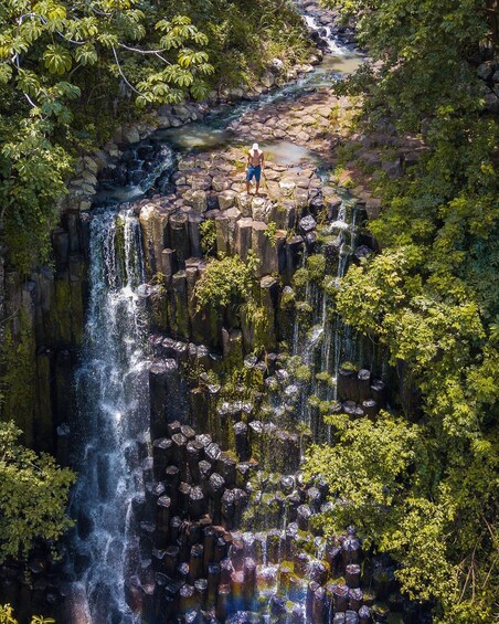 A waterfall cascading over a rocky ledge surrounded by dense greenery. 5