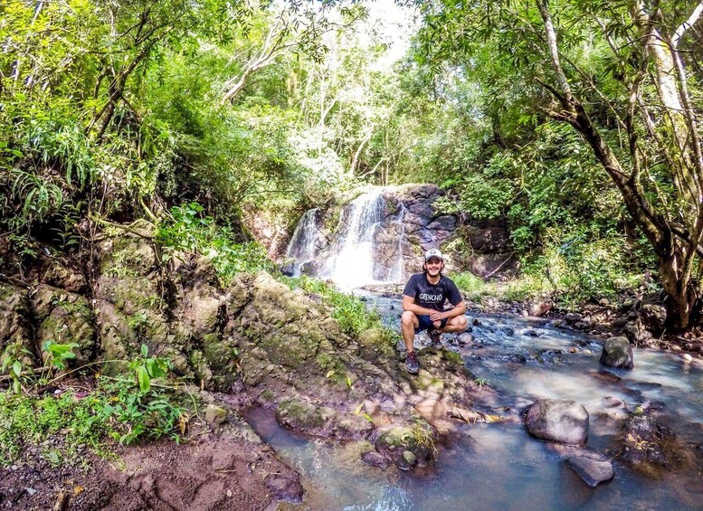 A person sitting by a small waterfall in a forested area. 4