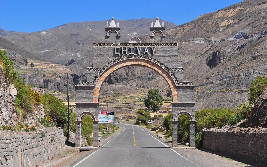A stone archway with 'CHIVAY' inscribed, leading to a road in a mountainous area. 2