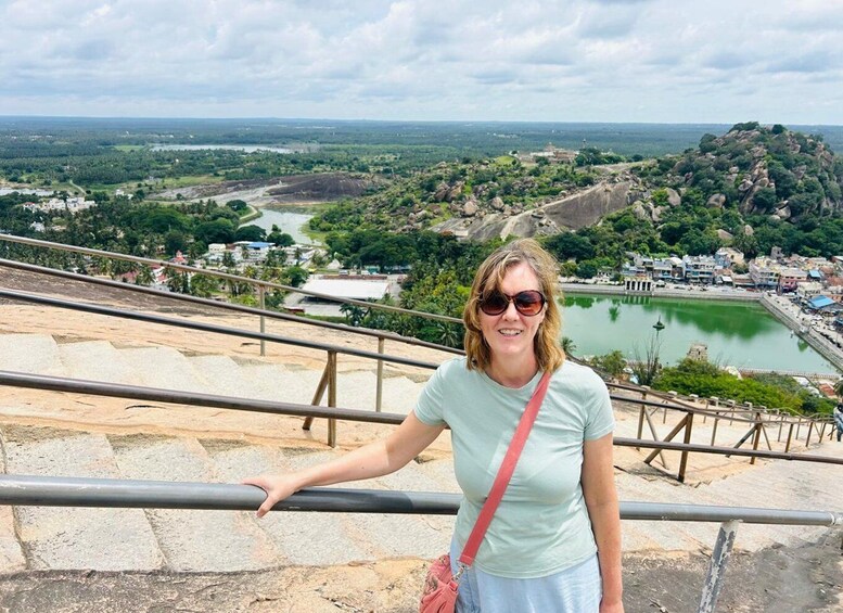 A person standing on a stone staircase overlooking a scenic landscape with a lake, buildings, and a hill. 2