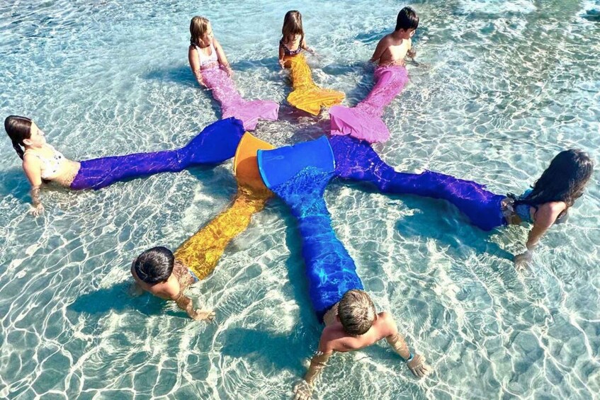People in a circle in a shallow pool with colorful mermaid tails. 5