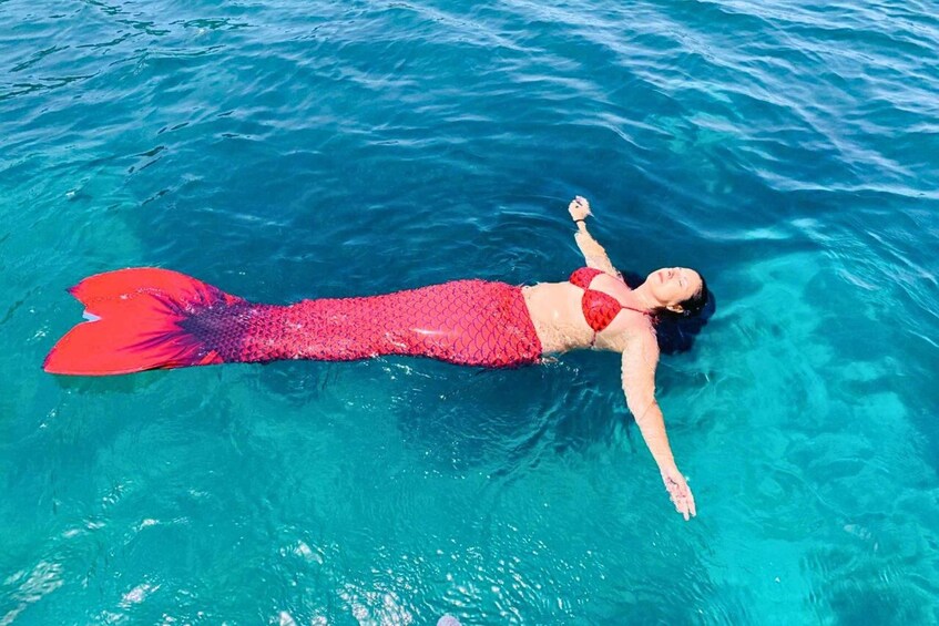 A person in a mermaid costume swimming in clear blue water. 5