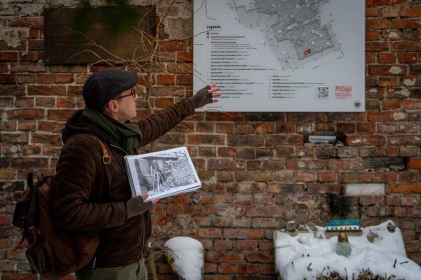 A person pointing at a map on a brick wall, holding a booklet. 5