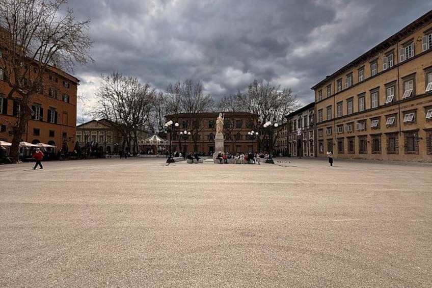 An open square with buildings, a statue, and a cloudy sky. 4