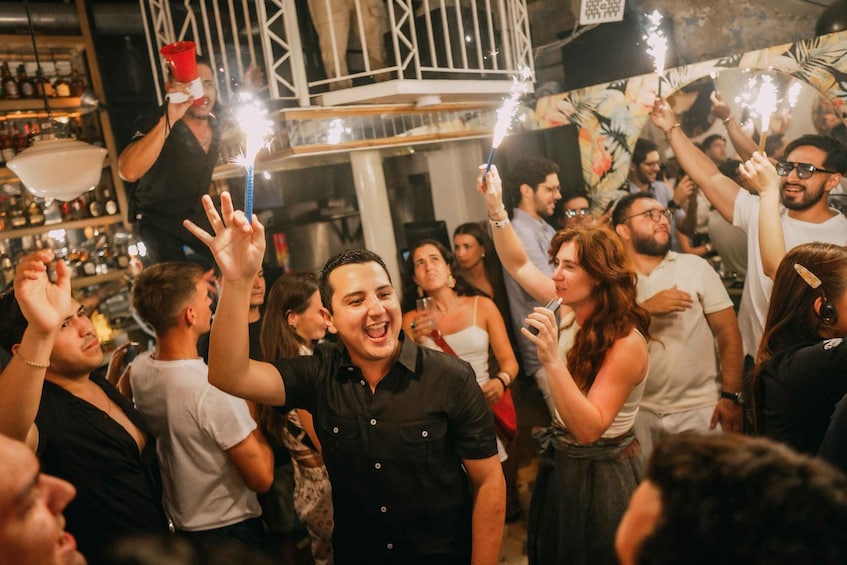 A crowded indoor party with people holding sparklers. 3