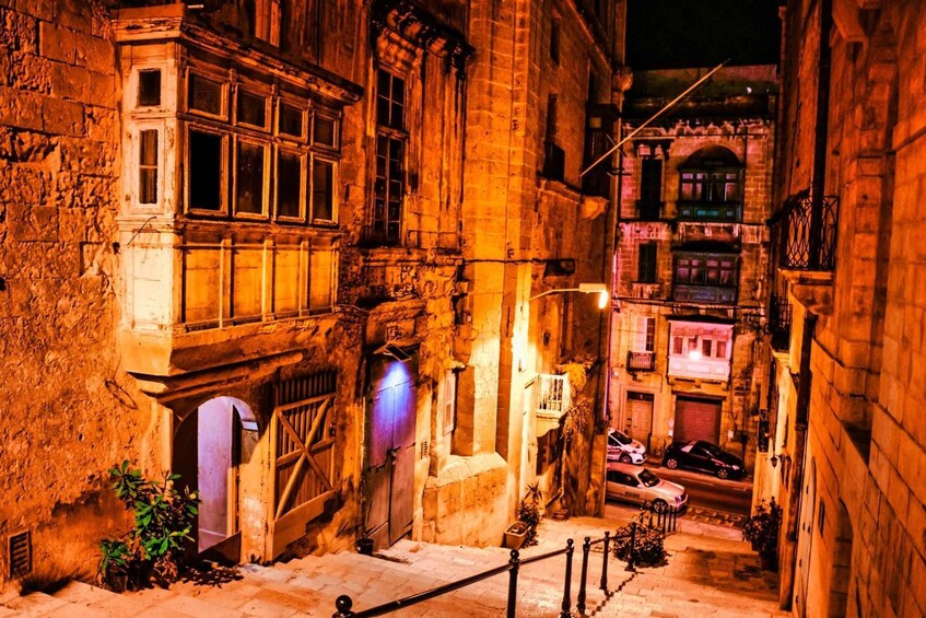 A narrow street with stone buildings, a wooden gate, and parked cars. 2