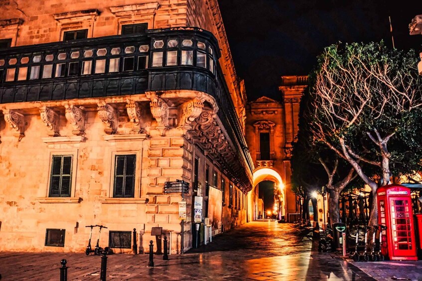 A historic building with ornate architecture, a red telephone booth, and a tree-lined street at night. 4