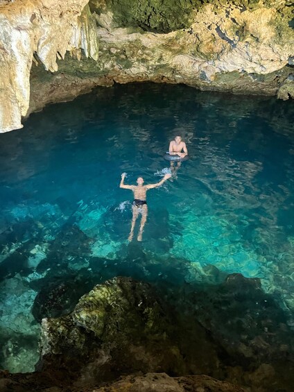 Two people swimming in a clear blue pool with rocky walls. 2
