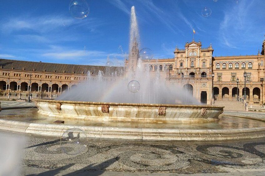 Une fontaine historique avec des jets d’eau, entourée d’un bâtiment classique doté d’arcades et d’une tour horloge. 1