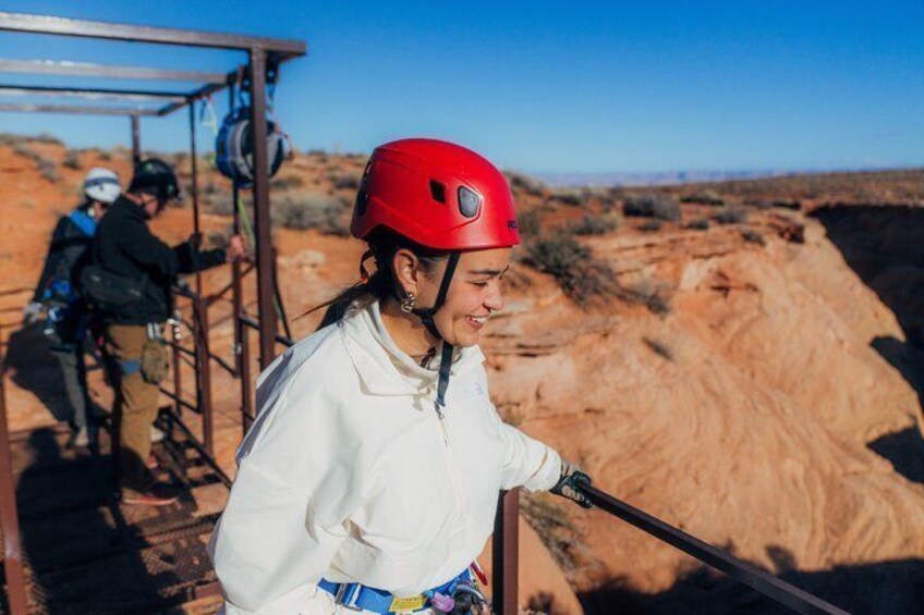 A person in a white jacket and red helmet standing on a metal structure with a desert landscape in the background. 3