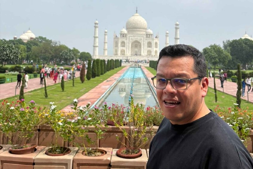A person standing in front of the Taj Mahal with a pool and garden in the foreground. 4
