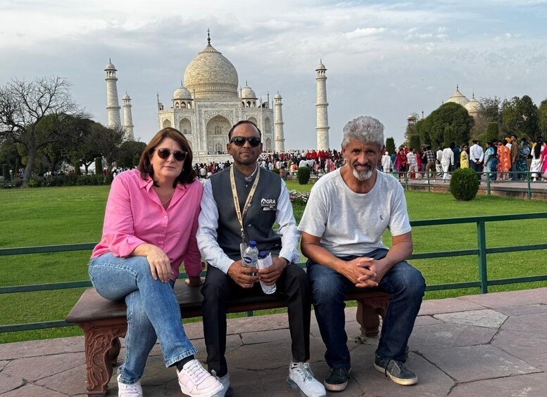 Three people sitting on a bench with the Taj Mahal in the background. 3