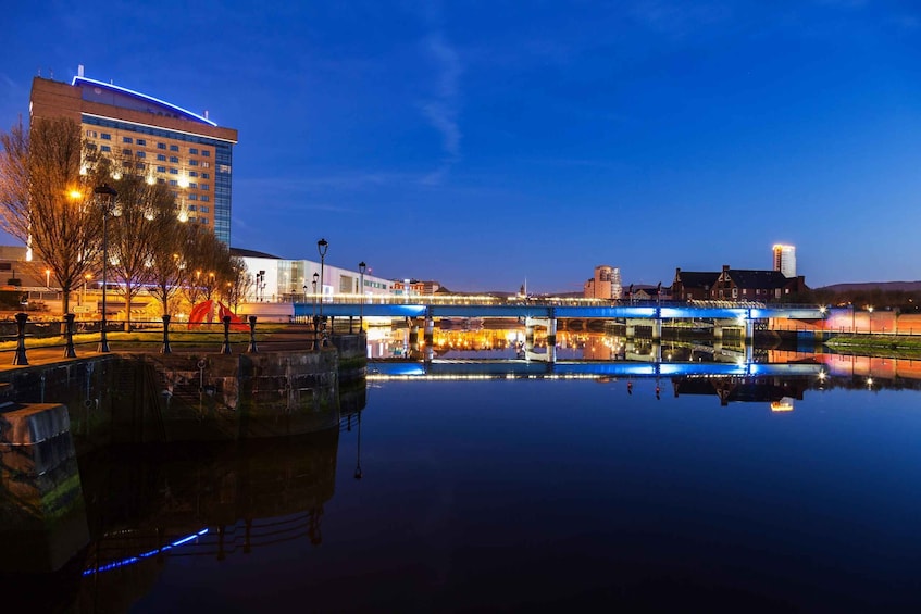 A cityscape at dusk with a river reflecting buildings and a bridge. 5