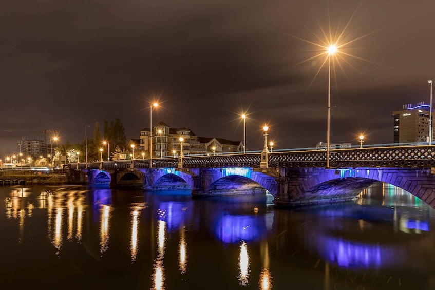 A nighttime view of a bridge with illuminated arches reflecting on the water. 3