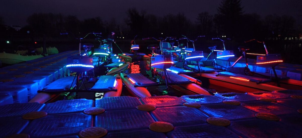A nighttime scene with multiple boats illuminated by colorful LED lights. 1