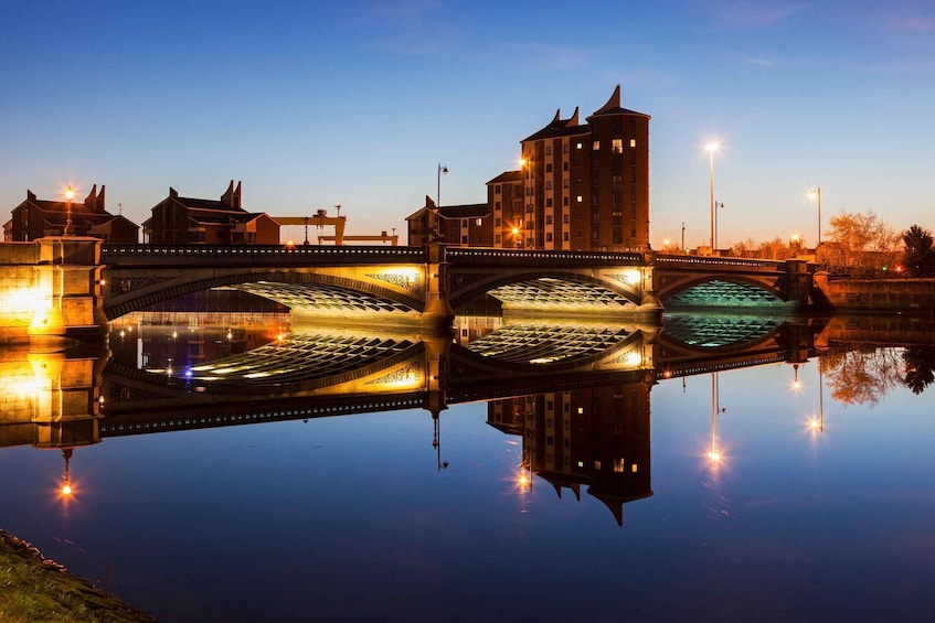 A bridge with illuminated arches over a calm river, reflecting the surrounding buildings and sky. 4