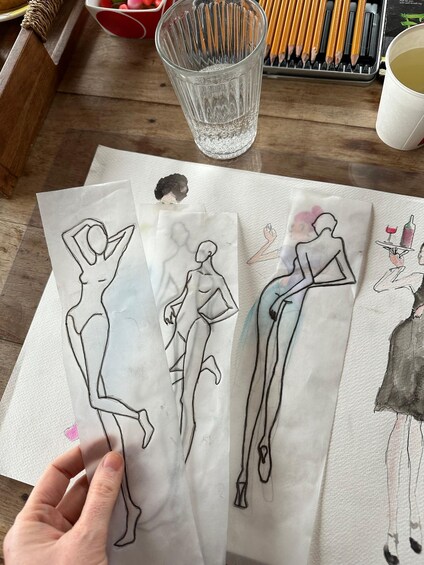 Three paper sketches of human figures on a wooden table. 5