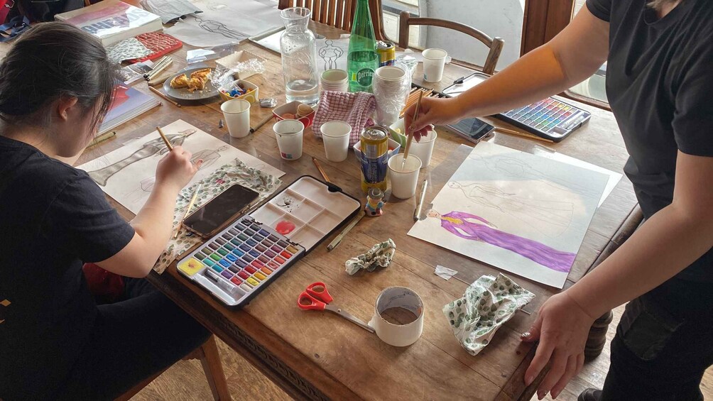 A person painting a figure on a canvas, with art supplies and a smartphone on the table. 4