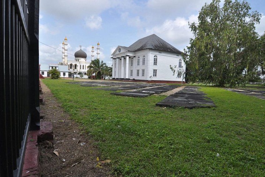 A white building with a dome and minarets, a grassy area with a paved path, and a tree. 4