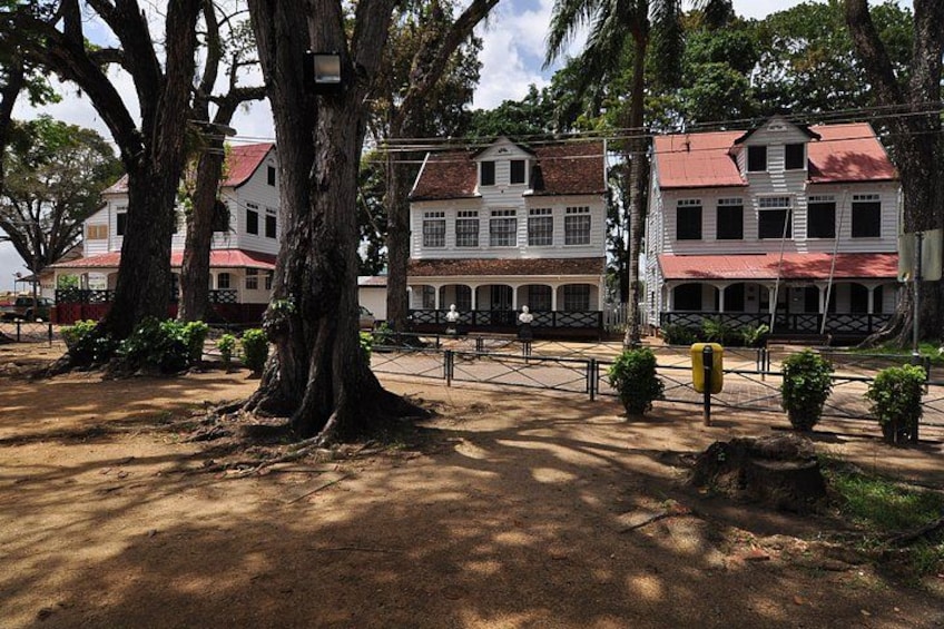 A colonial-style building with a red roof, surrounded by large trees and a paved area. 3