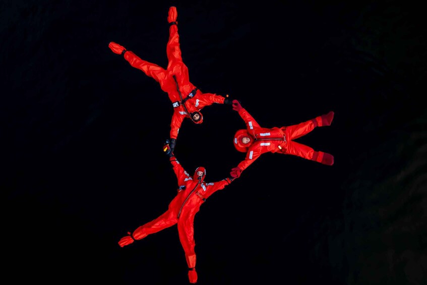 Three individuals in red suits performing an aerial maneuver against a dark background. 1