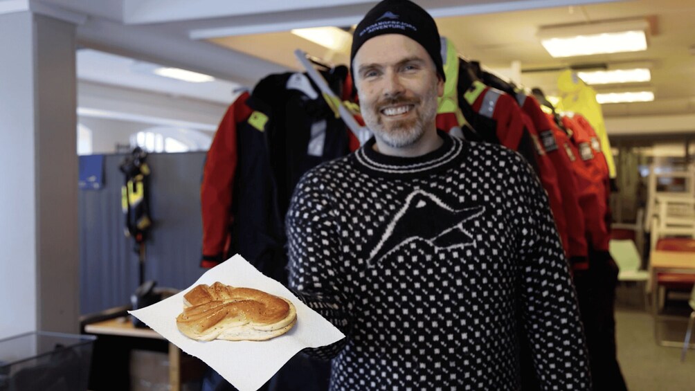A person holding a bagel in a store with jackets hanging in the background. 3