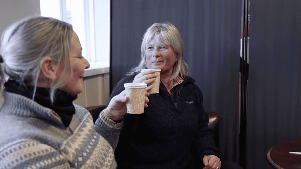 Two people sitting indoors, one holding a patterned paper cup. 5