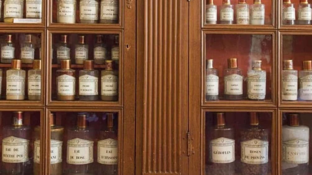 A wooden cabinet with multiple glass-fronted shelves containing bottles of perfume. 5