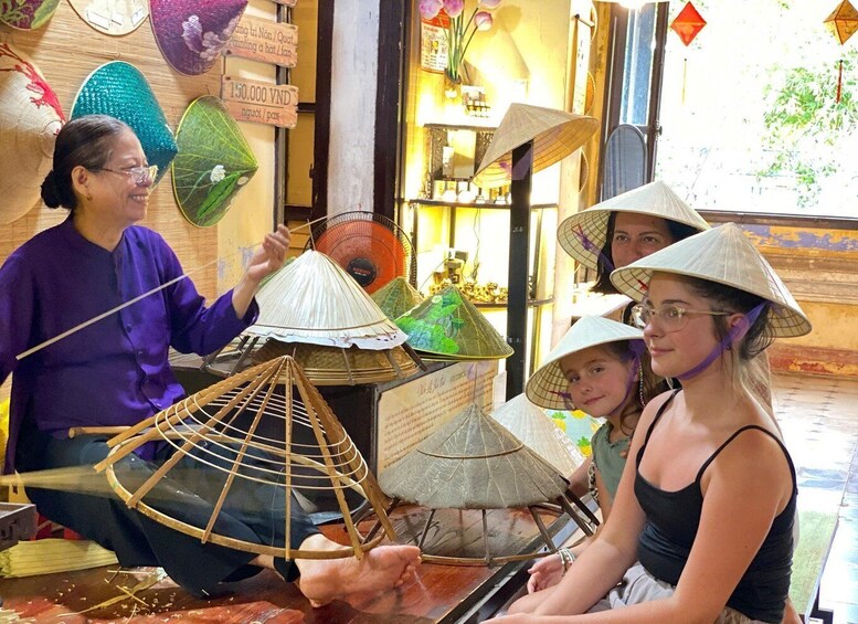 Una persona mostrando el uso de un sombrero cónico tradicional, con varios otros sombreros cónicos exhibidos al fondo. 3