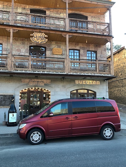 A red minivan parked in front of a building with a sign that reads "Hotel Adlig Alten Zentrum." 2