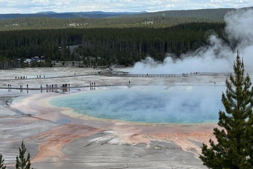 A geothermal area with mineral deposits, a visitor center, and a forested background. 3