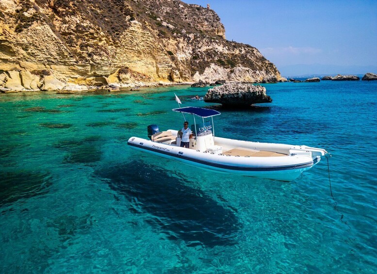 A boat anchored near a rocky coastline with clear turquoise water. 1