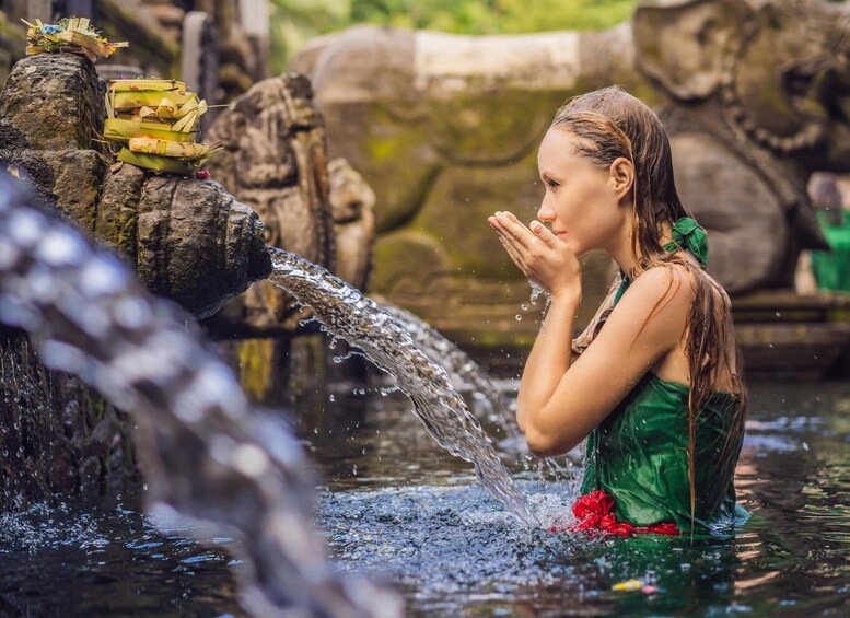A person in a green dress standing in water with a waterfall. 1