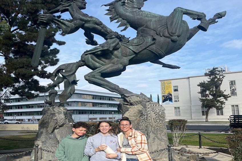 Eine bronzene Reiterstatue, vor der drei Personen stehen. 2