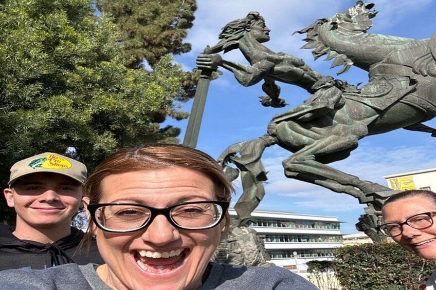 Una estatua ecuestre de bronce con un jinete y un caballo, un edificio al fondo y un cielo despejado. 1