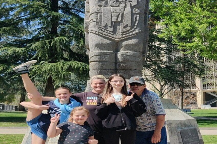 Un grupo de personas posando frente a un monumento de piedra con un escudo. 4