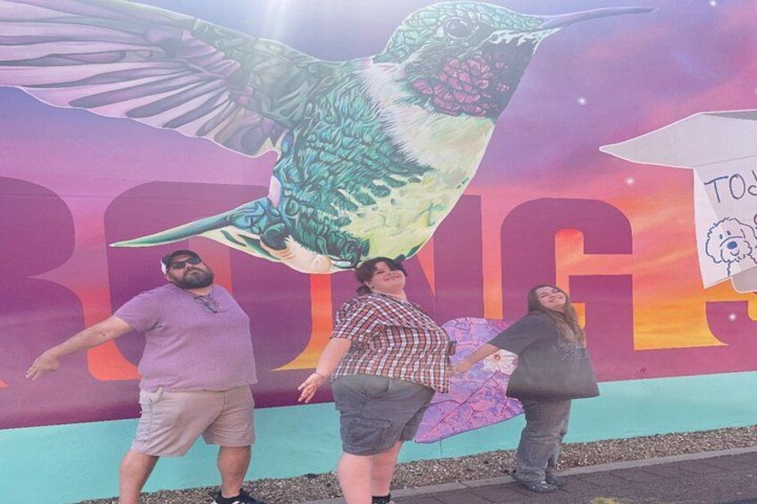 Tre personer foran en farverig mural med en stor fugl og ordet 'BRING'. 5