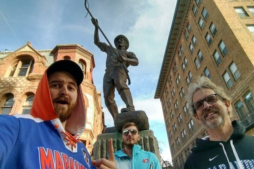 Three people standing in front of a statue and a building. 5