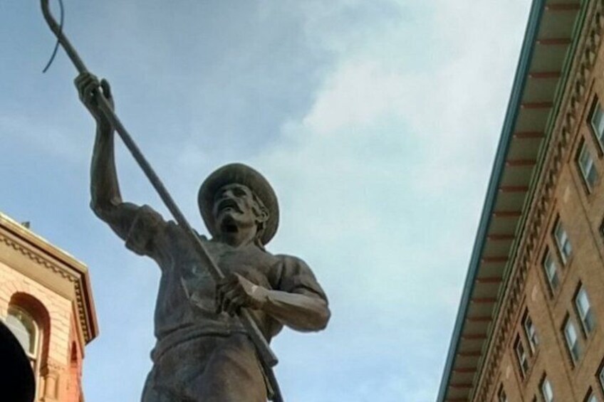 A statue of a person holding a staff, with buildings in the background. 2