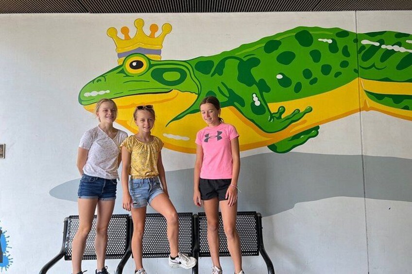 Three people sitting on a bench with a large frog mural behind them. 2