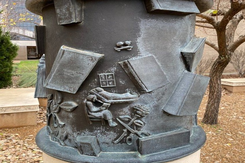 A sculpture with a figure of a person reading a book, surrounded by books and a globe. 4