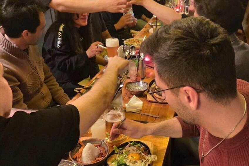 Mensen zitten aan een tafel, proosten met drankjes en delen eten. 2
