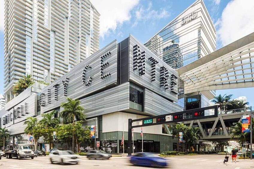 A modern building with large signage, surrounded by palm trees and other urban structures. 1